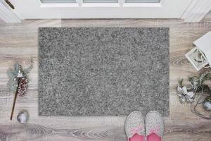 Blank grey doormat before the door in the hall. Mat on wooden floor, with christmas decoration and slippers. Welcome home, product Mockup photo