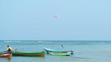 PHUKET, THAILAND NOVEMBER 13, 2019 - AirAsia Airbus A320 approaching over ocean and Longtail fishers boats parked in Mai Khao beach near fishers village in Phuket island. Thailand video