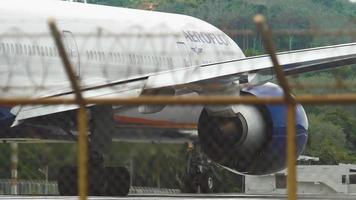 phuket, thailand 26 november 2017 - een aeroflot-passagiersboeing 777 bereidt zich voor op het opstijgen op de luchthaven van phuket aan het begin van de landingsbaan. zicht op het vliegtuig door het hek video