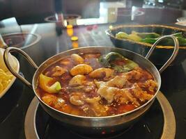 Chinese hot pot with spicy broth in bowl with meat and vegetables photo