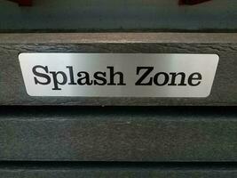 metal splash zone sign on wood fence near water photo