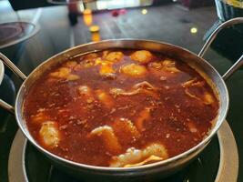 olla caliente china con caldo picante rojo en un tazón en la mesa foto