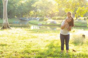 Beautiful young asian mother carrying little daughter with smile, child ride the neck on mom with happiness and cheerful together in the park, lifestyle family with enjoy and fun concept. photo