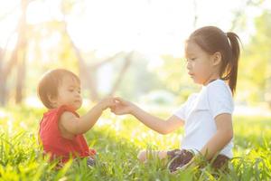 hermoso niño asiático joven sentado jugando en verano en el parque con disfrute y alegre en la hierba verde, actividad infantil con relajación y felicidad juntos en el concepto de pradera, familia y vacaciones. foto