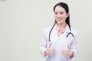 Asian young woman doctor who wears medical uniform is showing hand as thump up on white background. photo