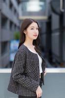 Portrait of a beautiful, long-haired Asian female side face in a black pattern coat with braces on teeth standing and smiling outdoors in the city. photo
