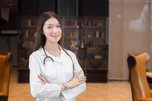 Professional young age Asian woman doctor standing smile in a good mood with arms crossed in the office room in the hospital. Wearing a white robe and stethoscope. photo