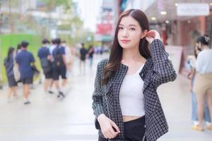 Portrait of a beautiful, long-haired Asian woman in a black gray pattern coat standing and smiling outdoors in the city. photo