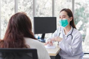 Asian elderly woman patient is checked health by professional doctor while both wear medical face mask at the examination room in hospital. photo