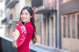 Beautiful Asian female in red dress stands holds a fan among old city center in Chinese new year theme. photo