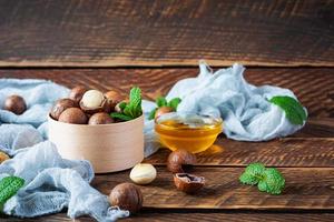 nueces de macadamia con cáscara con hojas de menta y miel sobre fondo de madera foto