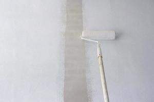 Long handle roller brush applying primer white paint on cement wall background, buildind and home renovation concept photo