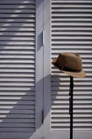 luz solar y sombra en la superficie del sombrero fedora con bastón de metal sobre fondo de pared plegable de madera blanca en estilo de tono vintage y marco vertical foto