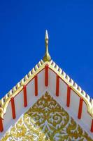 Low angle view of golden gable apex on ornamental Thai temple roof against blue clear sky background in vertical frame photo