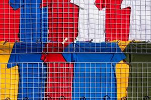 Rows of many multi colored T-shirts hanging on white grille mesh clothes rack for sale in clothing store in outdoor market photo