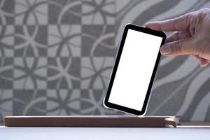 Close up man's hand showing smartphone with blank screen in leaning gesture on book with blurred abstract pattern on brown tile wall background photo