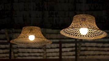 Focus on foreground of 2 vintage hanging lamps decoration with bamboo farmer's hat against straw thatched roof inside of traditional hut photo