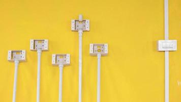 White plastic light switch box with pipe line and electric socket boxes on yellow cement wall background inside of house construction site photo