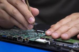 Close up and selective focus at mini screw on green mainboard with part of technician's hand in assembling the motherboard of laptop computer at workshop photo