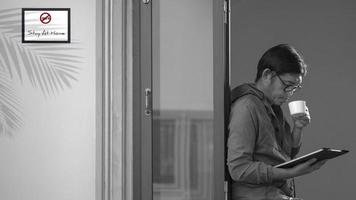 Asian man drinking hot coffee and looking at clipboard in glass window frame at home in self-isolation concept photo