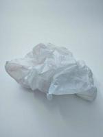 A crumpled white plastic bag lying on a white background is a disposable material that pollutes the world's ecosystems. photo