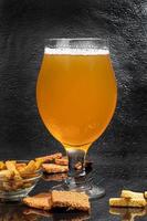 Glasses with different types of craft beer on a wooden bar. In glasses and bottles. Nuts and crackers on the table. On a dark background. photo