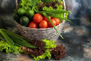 Fresh vegetables for salad in a basket. Tomatoes and cucumbers with zucchini and cabbage with dill. Spring harvest, benefits and vitamins. On a dark background. photo