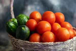 Fresh vegetables for salad in a basket. Tomatoes and cucumbers with zucchini and cabbage with dill. Spring harvest, benefits and vitamins. On a dark background. photo