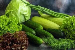 Fresh vegetables for salad. Tomatoes and lettuce, cucumbers with zucchini and cabbage with dill. Spring harvest, benefits and vitamins. On a dark background. photo