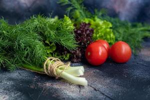 Fresh vegetables for salad. Tomatoes and lettuce, cucumbers with zucchini and cabbage with dill. Spring harvest, benefits and vitamins. On a dark background. photo
