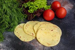 Sliced cheese with slices of tomatoes and bell peppers. Along with spring vegetables. On a dark background. photo