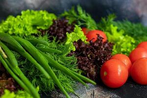Fresh vegetables for salad. Tomatoes and lettuce, cucumbers with zucchini and cabbage with dill. Spring harvest, benefits and vitamins. On a dark background. photo