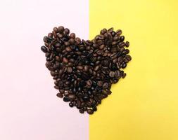Heart shape roasted coffee beans brown and dark seed variation on half pastel pink and yellow background photo