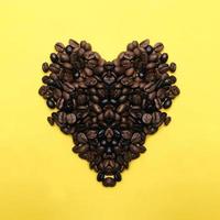 granos de café tostados en forma de corazón variación de semillas marrones y oscuras sobre fondo amarillo en el centro foto