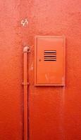 vertical metal pipe and electric box on orange color wall photo