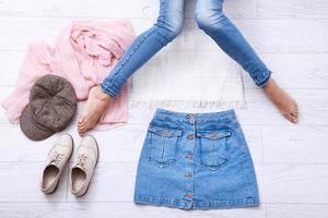 ropa casual de verano con diferentes accesorios y piernas femeninas en jeans sobre suelo de madera blanca. vista superior y espacio de copia. foto