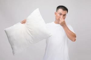 la almohada huele mal. retrato de un hombre asiático sosteniendo una almohada blanca y con mal olor. foto de estudio en gris