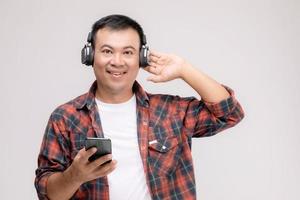 retrato de un hombre asiático escuchando una canción o música desde un auricular negro. tiro del estudio aislado en gris foto