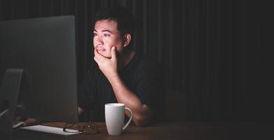 Early working in the morning concept, Asian man working on computer in the dark room and looking to screen with exciting face photo