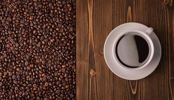 granos de café tostados y taza de café en textura de madera. vista superior textura de granos de café marrones para fondo y uso de papel tapiz foto