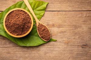 cierre el cacao en polvo en un tazón de madera y una hoja verde en una mesa de madera foto