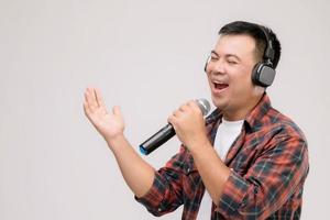 retrato de un hombre asiático escuchando una canción o música desde un auricular negro. tiro del estudio aislado en gris foto
