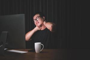 Neck pain or tired concept. Man touching his neck because pain or hurt after long time working on computer in the dark room at home photo