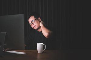 Neck pain or tired concept. Man touching his neck because pain or hurt after long time working on computer in the dark room at home photo