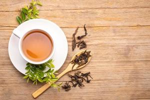 White cup of hot tea and dry tea leaf on wooden table photo