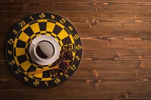 Cup of coffee on dart board on brown wooden table background. Composition with free space for text or design photo