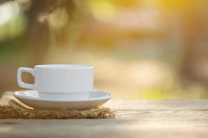 taza de café y granos de café en una mesa de madera al aire libre a la luz del sol de la mañana y fondo de bokek foto