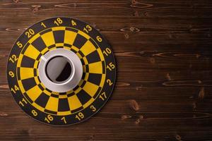 Cup of coffee on dart board on brown wooden table background. Composition with free space for text or design photo