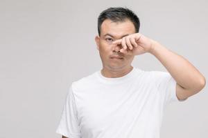 concepto de irritación ocular. retrato de un hombre asiático en postura de ojo cansado, irritación o problema con su ojo. tiro del estudio aislado en gris foto