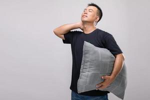 concepto de dolor de cuello, retrato de un hombre asiático sosteniendo una almohada gris y sintiéndose cansado o dolorido en el cuello. tiro del estudio aislado en gris foto